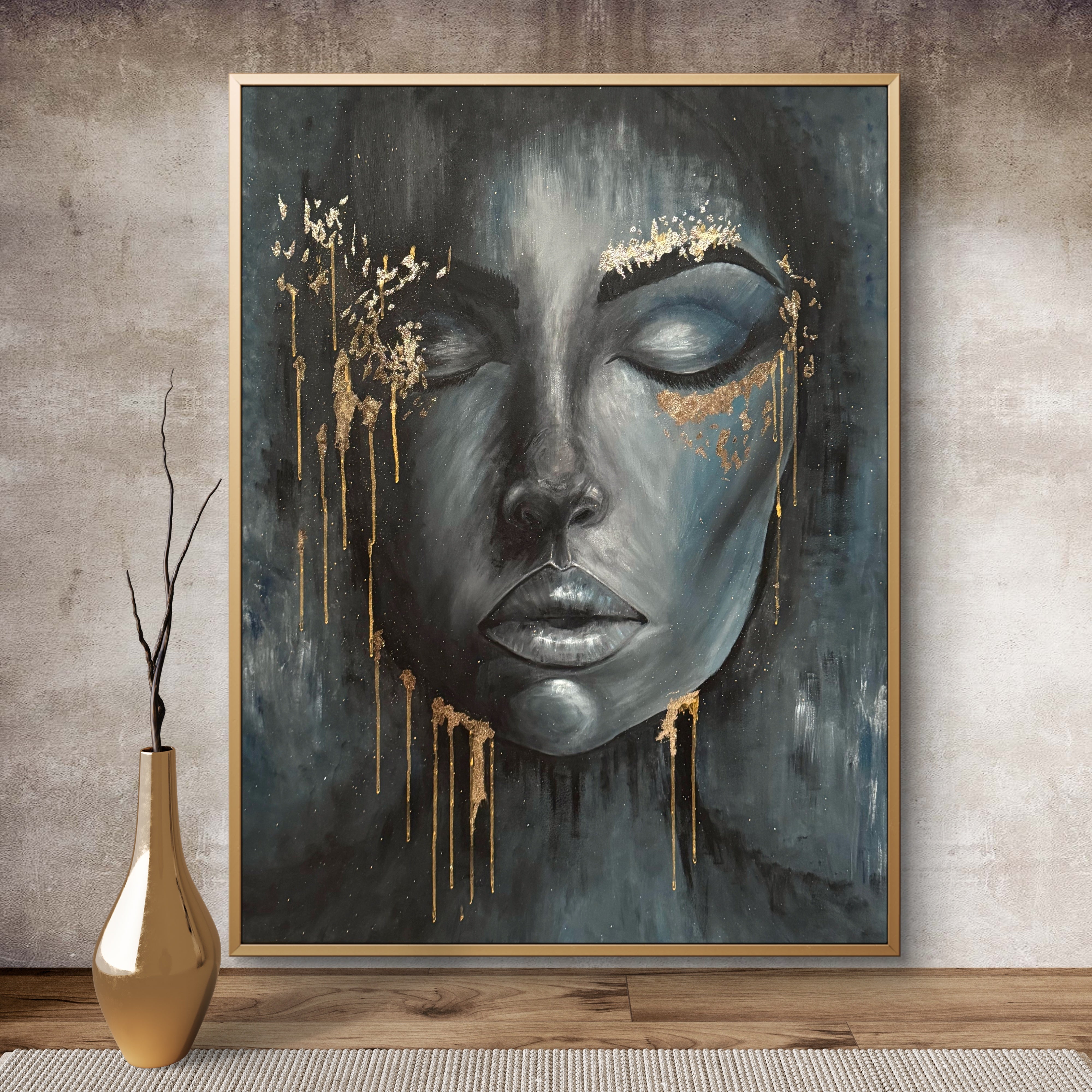Framed artwork of a stylized face with gold accents on a textured wall.