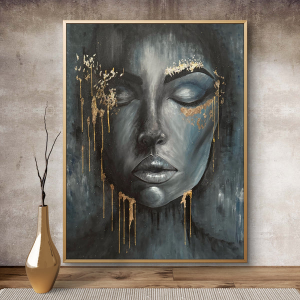 Framed artwork of a stylized face with gold accents on a textured wall.